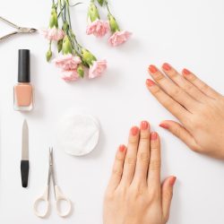 Female hands applying purple nail polish on wooden table with towel and nail set